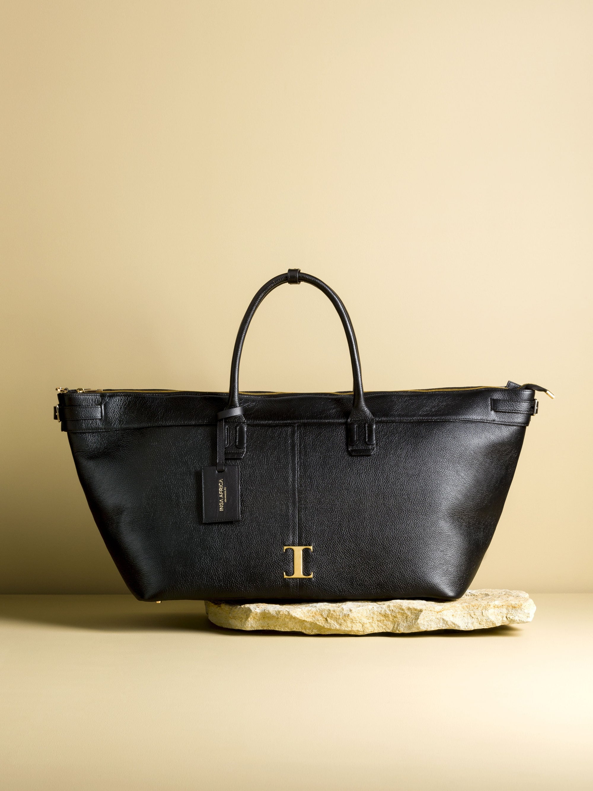 Black leather handbag with gold logo on a beige background